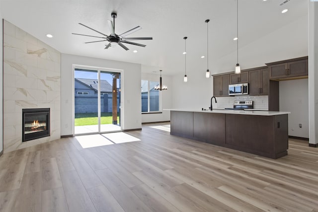 kitchen with dark brown cabinetry, sink, appliances with stainless steel finishes, pendant lighting, and a kitchen island with sink