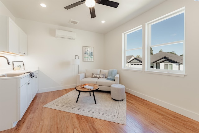 living room with sink, a wall unit AC, ceiling fan, and light wood-type flooring