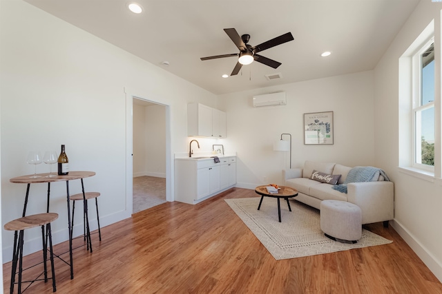 living area with a wall mounted air conditioner, light hardwood / wood-style flooring, sink, and ceiling fan