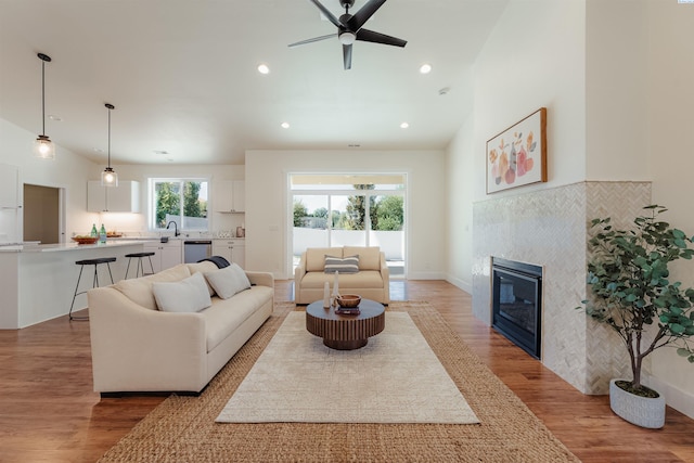 living room featuring a tile fireplace, high vaulted ceiling, sink, ceiling fan, and light hardwood / wood-style floors