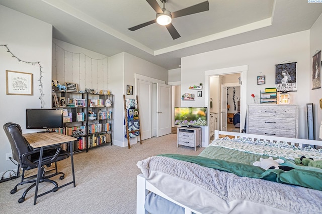 carpeted bedroom featuring an office area, ceiling fan, baseboards, and a raised ceiling
