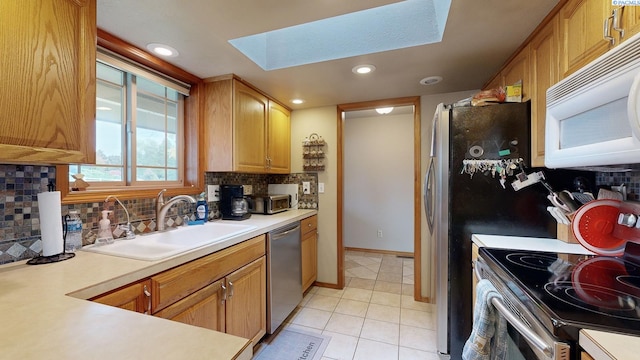 kitchen featuring sink, a skylight, light tile patterned floors, stainless steel appliances, and decorative backsplash