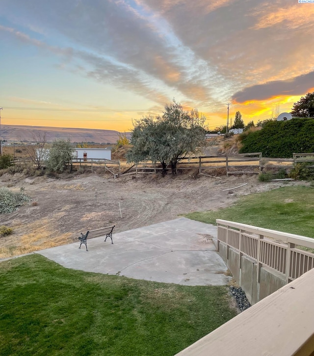 patio terrace at dusk featuring a mountain view and a lawn