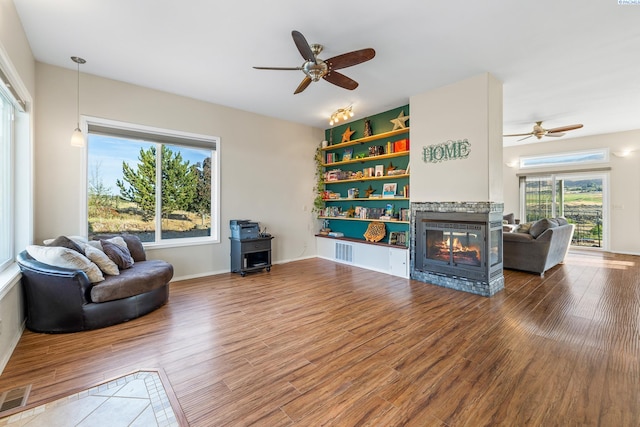 living room featuring wood-type flooring, a multi sided fireplace, and ceiling fan