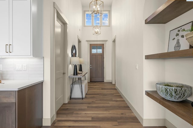 entrance foyer with an inviting chandelier, plenty of natural light, baseboards, and dark wood finished floors