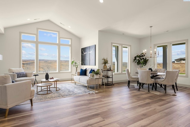 living area with a healthy amount of sunlight, vaulted ceiling, an inviting chandelier, and wood finished floors