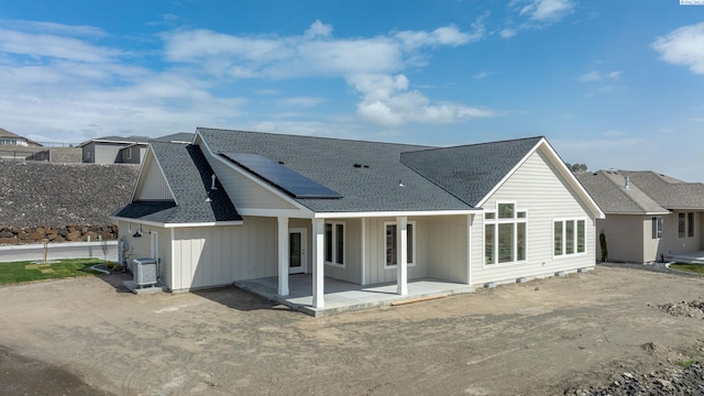 back of house with cooling unit, solar panels, roof with shingles, board and batten siding, and a patio area