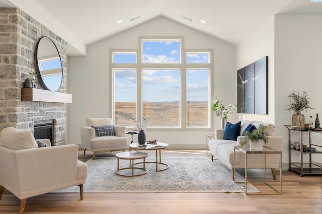 living area with recessed lighting, visible vents, a stone fireplace, wood finished floors, and high vaulted ceiling