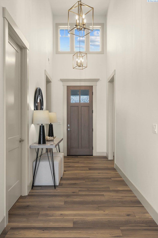 foyer with wood finished floors, a towering ceiling, baseboards, and an inviting chandelier