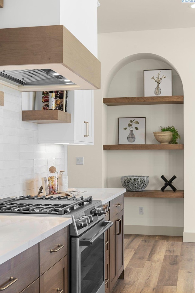 kitchen featuring gas range, light countertops, light wood-style floors, premium range hood, and open shelves