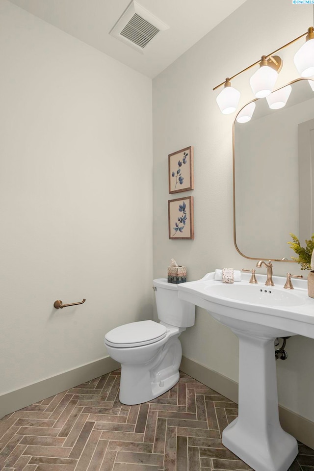 half bath featuring toilet, visible vents, and baseboards