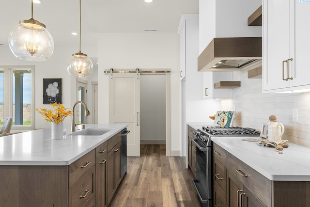 kitchen featuring backsplash, a barn door, appliances with stainless steel finishes, a sink, and premium range hood