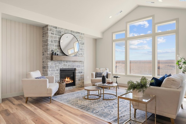 living room with recessed lighting, visible vents, a stone fireplace, wood finished floors, and high vaulted ceiling