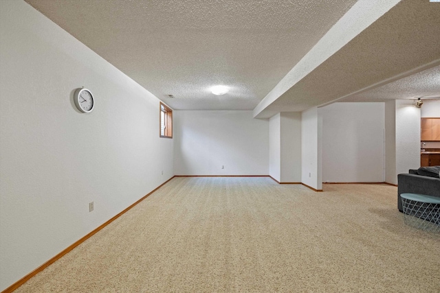 finished basement featuring a textured ceiling, light carpet, and baseboards