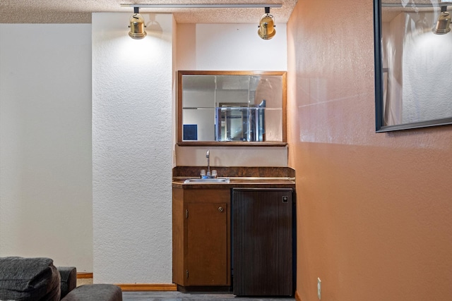 bar featuring a textured ceiling, a sink, a textured wall, and wet bar