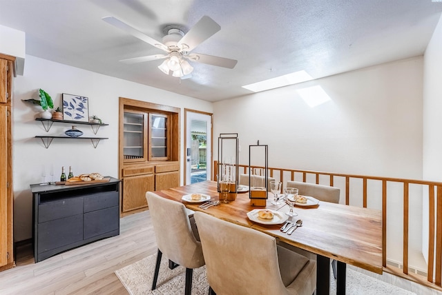 dining room featuring a skylight, a ceiling fan, and light wood-style flooring