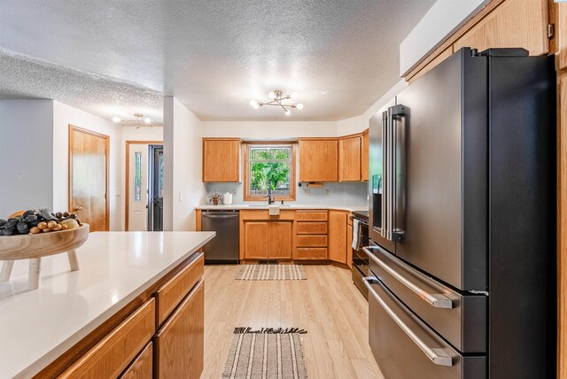 kitchen with appliances with stainless steel finishes, a textured ceiling, light wood-type flooring, and light countertops