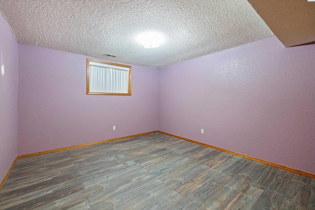 empty room featuring a textured ceiling, wood finished floors, and baseboards