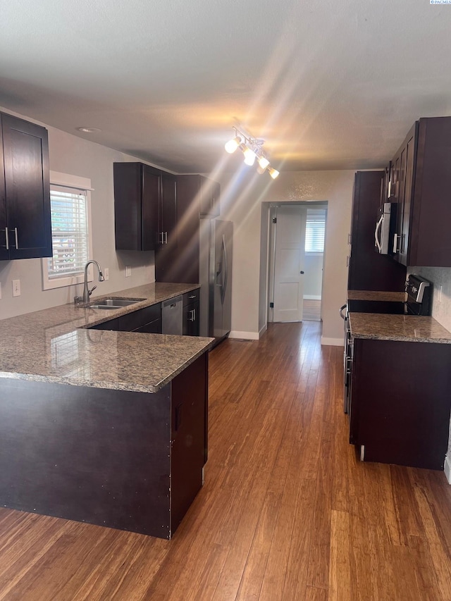 kitchen featuring dark wood-style flooring, a peninsula, stainless steel appliances, stone counters, and a sink