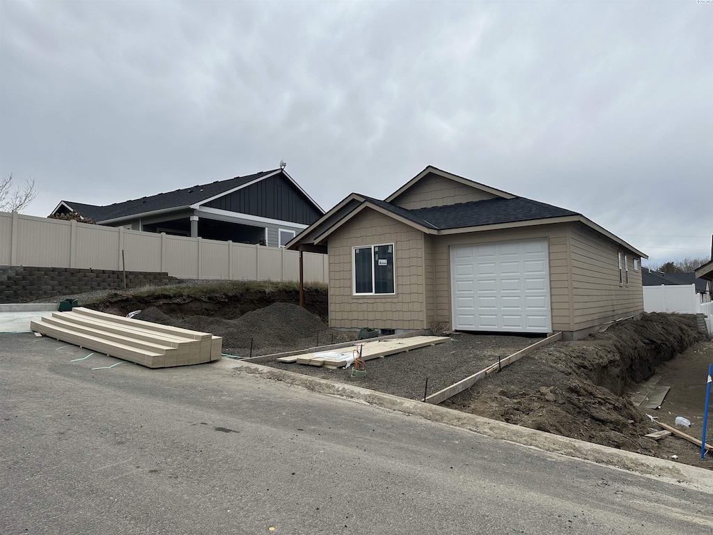 view of front of house featuring an attached garage, a shingled roof, and fence