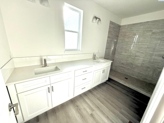 bathroom with double vanity, tiled shower, a sink, and wood finished floors