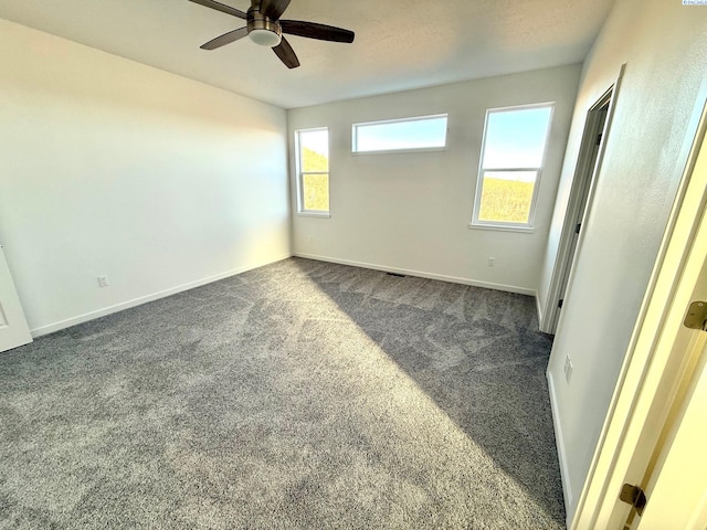 unfurnished room with baseboards, dark colored carpet, and a ceiling fan