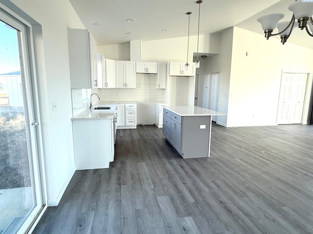 kitchen featuring a sink, a kitchen island, white cabinets, light countertops, and pendant lighting