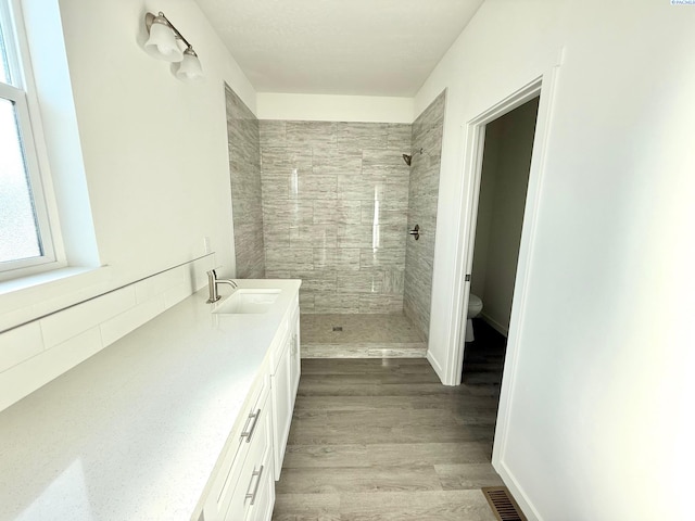 full bathroom with visible vents, tiled shower, wood finished floors, and toilet