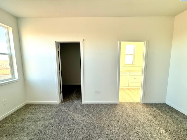 unfurnished bedroom with dark colored carpet, multiple windows, a walk in closet, and baseboards