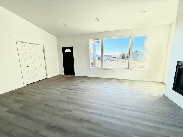 unfurnished living room featuring lofted ceiling, baseboards, wood finished floors, and a glass covered fireplace