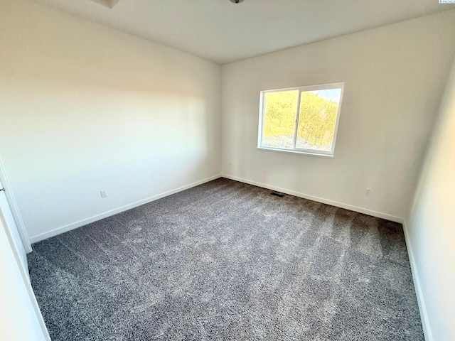 empty room with dark colored carpet, visible vents, and baseboards