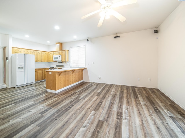 kitchen with kitchen peninsula, white appliances, ceiling fan, dark wood-type flooring, and a kitchen bar