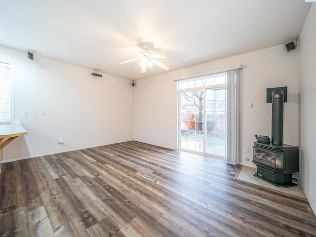 unfurnished living room featuring ceiling fan, a wood stove, and wood-type flooring