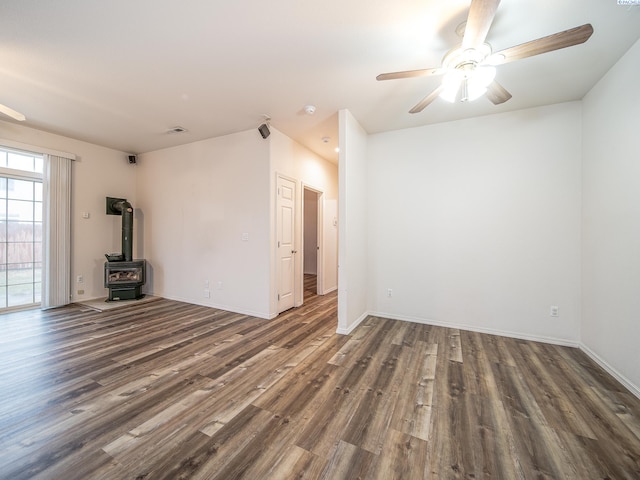 unfurnished room featuring a wood stove, dark wood-type flooring, and ceiling fan