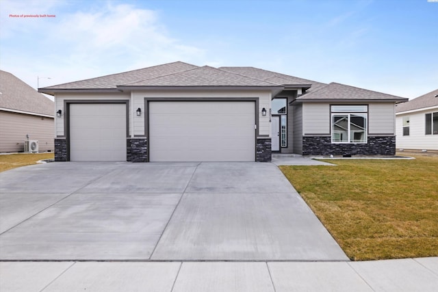 prairie-style house featuring roof with shingles, concrete driveway, a garage, stone siding, and a front lawn