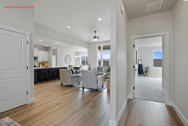 interior space with light wood finished floors, recessed lighting, visible vents, baseboards, and ceiling fan with notable chandelier