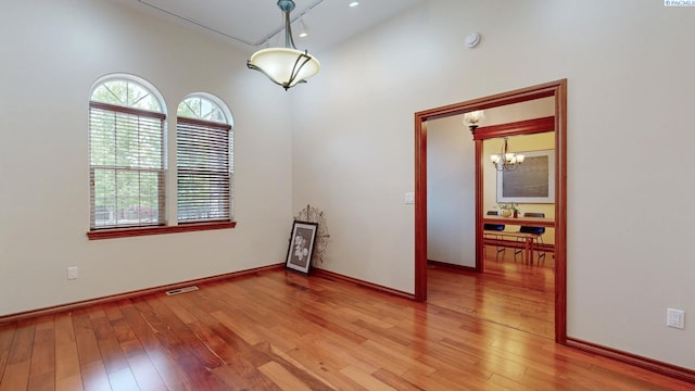 unfurnished room with light wood-type flooring, a chandelier, and baseboards
