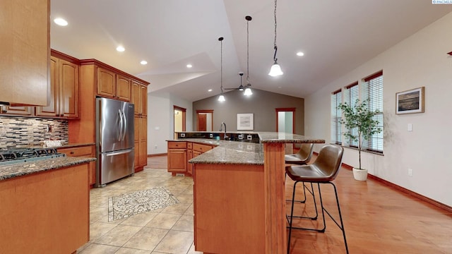 kitchen featuring appliances with stainless steel finishes, vaulted ceiling, a kitchen breakfast bar, backsplash, and a sink