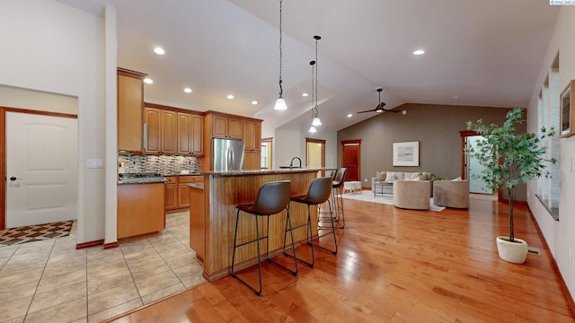 kitchen featuring freestanding refrigerator, ceiling fan, lofted ceiling, open floor plan, and a kitchen island with sink