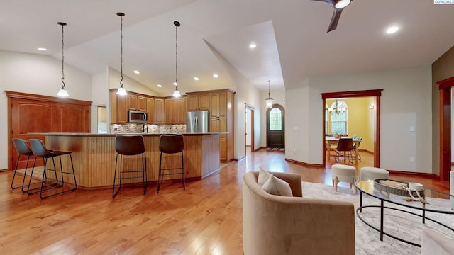 kitchen featuring stainless steel appliances, a kitchen bar, decorative backsplash, light wood-style floors, and vaulted ceiling