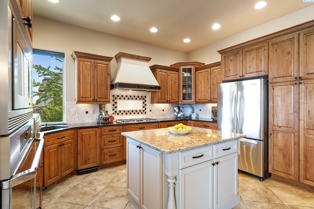 kitchen with brown cabinetry, recessed lighting, custom range hood, a sink, and appliances with stainless steel finishes
