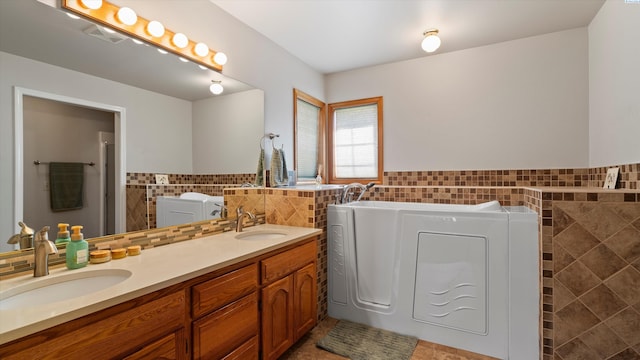 151002 W Richards Rd, Prosser, WA 99350 - bathroom featuring tile walls, washing machine and dryer, double vanity, a garden tub, and wainscoting