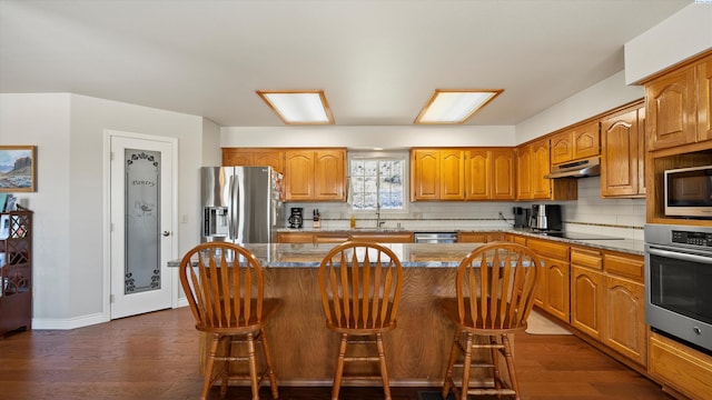 151002 W Richards Rd, Prosser, WA 99350 - kitchen featuring appliances with stainless steel finishes, under cabinet range hood, decorative backsplash, and dark wood-style flooring