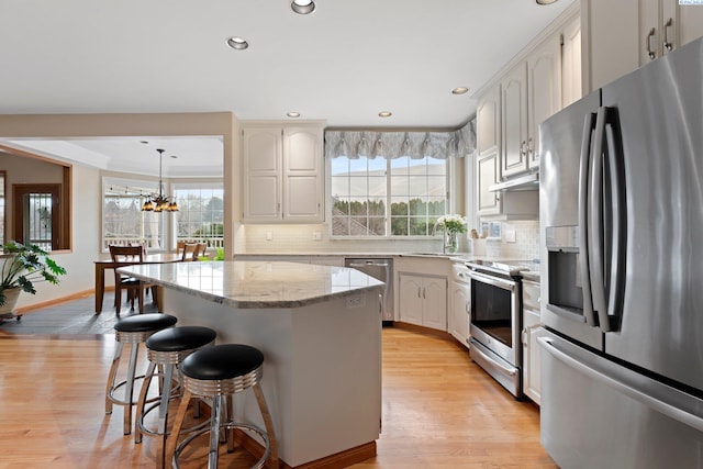 kitchen with white cabinetry, a center island, hanging light fixtures, light hardwood / wood-style flooring, and stainless steel appliances