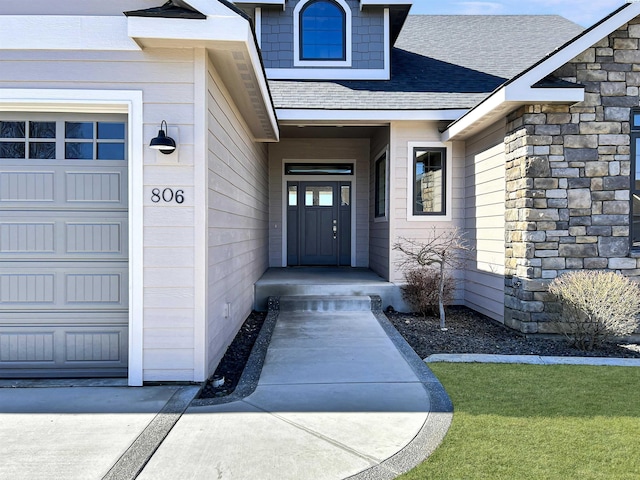 doorway to property with a garage, stone siding, and a shingled roof