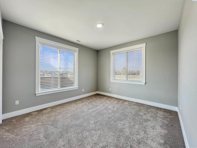 empty room featuring carpet floors, a wealth of natural light, visible vents, and baseboards