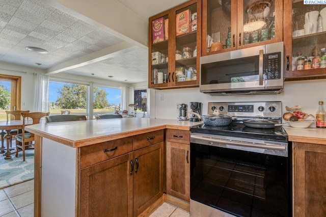 1706 Gaillard Pl, Richland, WA 99354 - kitchen with stainless steel appliances, a peninsula, light countertops, light tile patterned floors, and glass insert cabinets