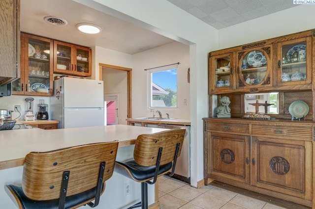 1706 Gaillard Pl, Richland, WA 99354 - kitchen featuring freestanding refrigerator, brown cabinetry, light tile patterned floors, a sink, and glass insert cabinets