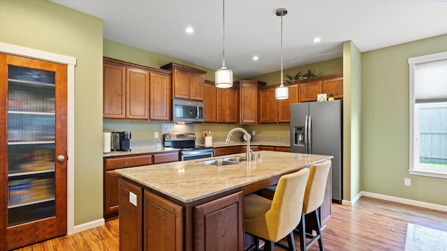 6102 Westmoreland Ln, Pasco, WA 99301 - kitchen with appliances with stainless steel finishes, light wood-style flooring, a center island with sink, light stone counters, and hanging light fixtures