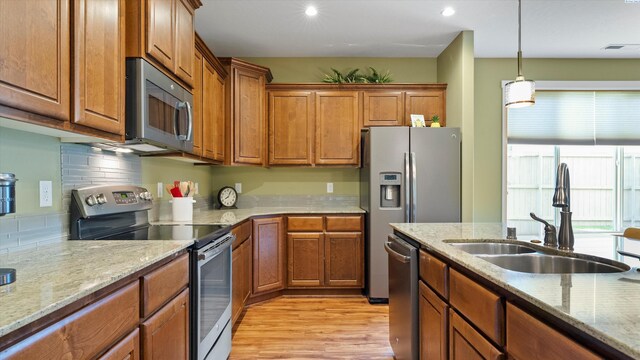 6102 Westmoreland Ln, Pasco, WA 99301 - kitchen with stainless steel appliances, brown cabinetry, light wood-style flooring, hanging light fixtures, and light stone countertops